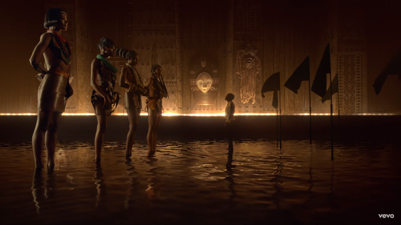 Kendrick Lamar stands on the flooded floor of a golden room looking up to four gigantic women, the goddesses of the temple. 