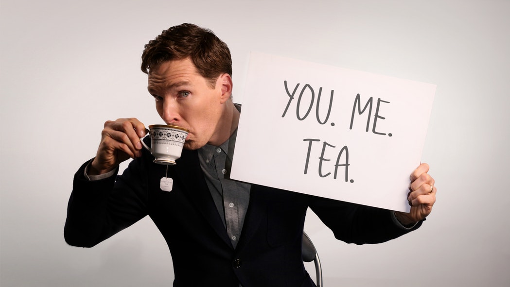 Benedict Cumberbatch sipping tea from an ornate teacup and holding a sign that reads, "You. Me. Tea."