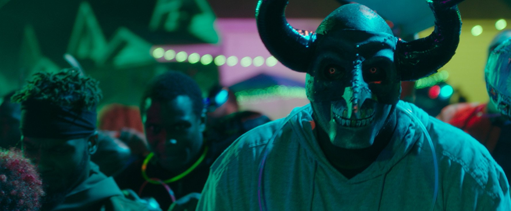 A person in a scary horned mask is in the foreground as black men are possibly partying amid a disturbing color scheme.