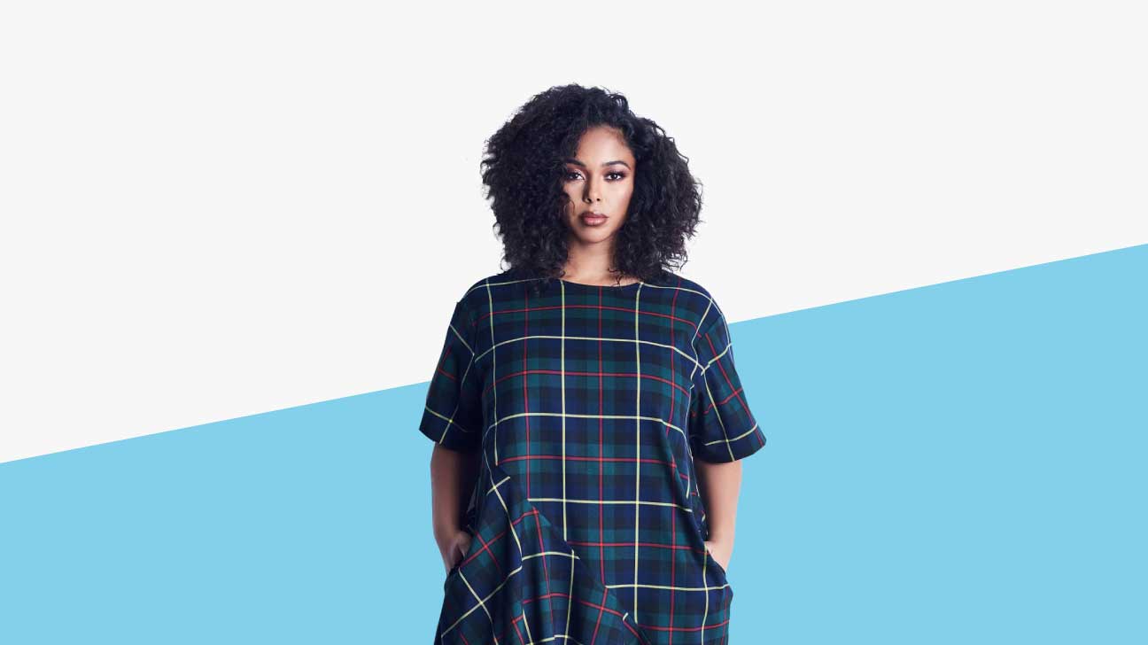 Black plus sized model with curly hair wearing a blue, grey, and forest green large plaid dress