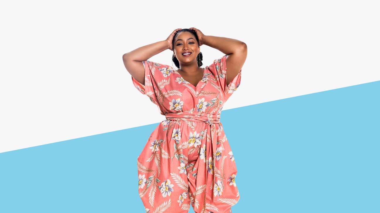 A black plus-sized model is wearing a pink jumpsuit with a white and blue floral print. 
