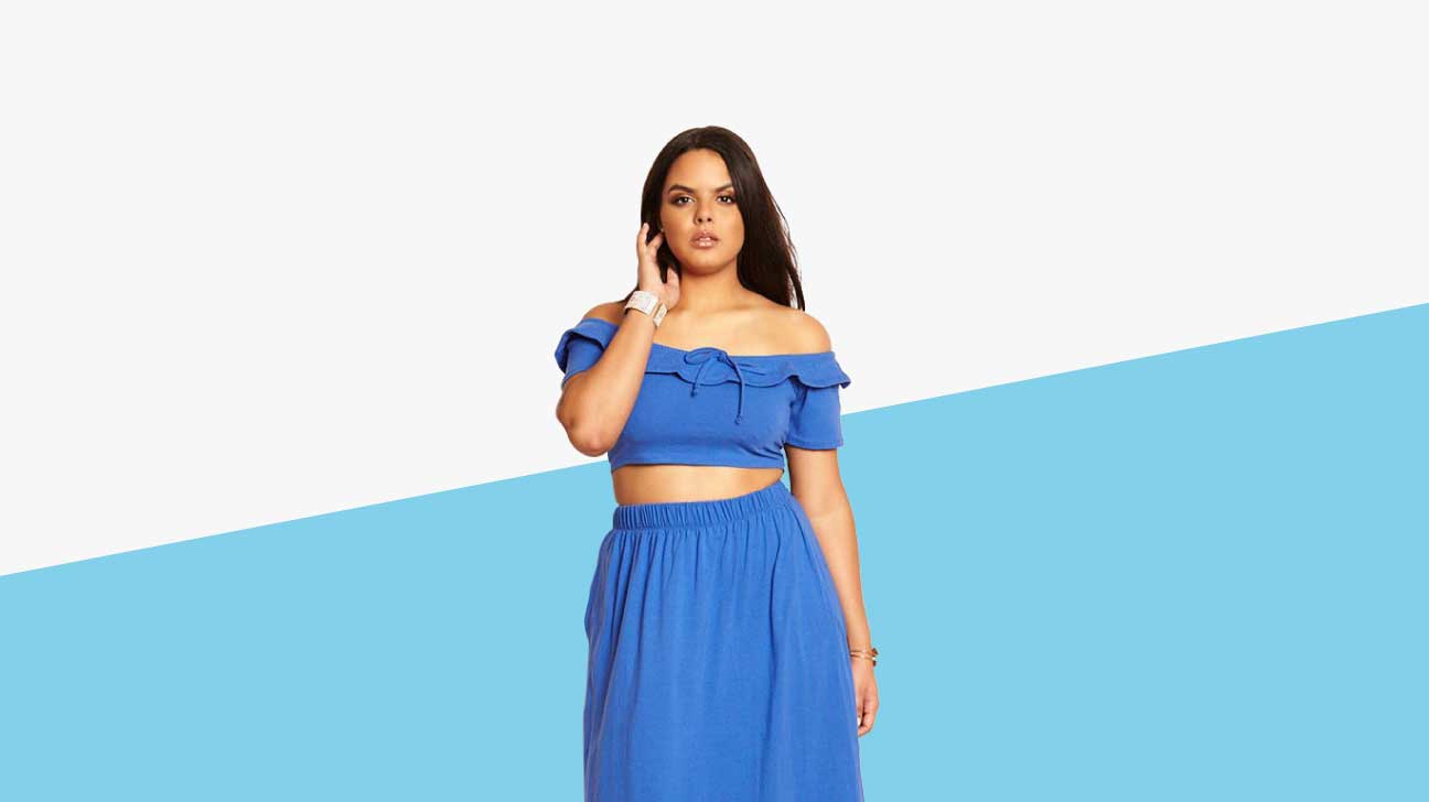 A light-skinned plus sized model is wearing a blue ruffledcropped peasant top and matching skirt set. 
