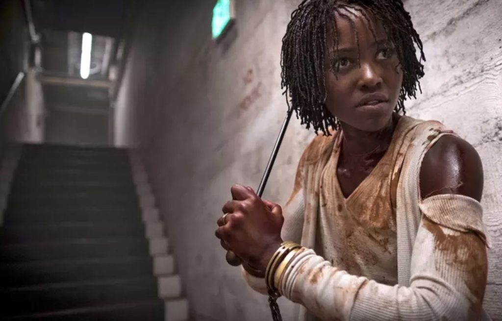 Lupita Nyong'o, bloodied, walks down stairs holding a fire poker.