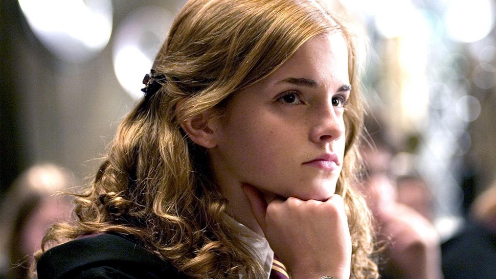 Hermione Granger rests her chin on her closed fits as she looks into the distance while sitting at a table in Hogwarts.