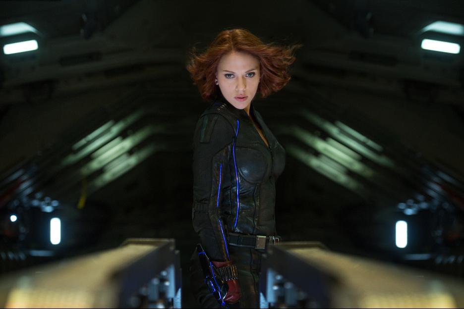 Black Widow stares down the barrel of something dangerous as her hair blows in the wind. She's in some kind of dark hangar. 