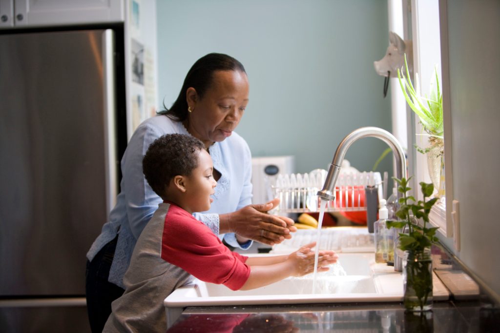 This African-American mother was shown in the process of teaching her young son how to properly wash his hands at their kitchen sink, briskly rubbing his soapy hands together under fresh running tap water, in order to remove germs, and contaminants, thereby, reducing the spread of pathogens, and the ingestion of environmental chemicals or toxins. Children are taught to recite the Happy Birthday song, during hand washing, allotting enough time to completely clean their hands. Keeping your hands clean is especially important during the COVID-19 outbreak. 
