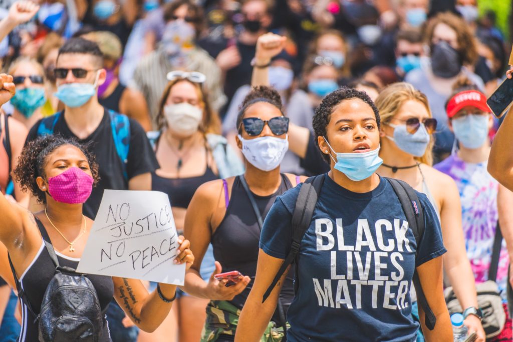 Picture of a revolution. A young woman wearing a mask and black lives matter t-shirt marching in a #BlackLivesMatter public demonstration in Cincinnati. Photo by Julian Wan on Unsplash