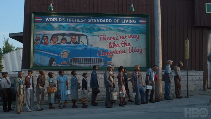 The two Americas, a line of Black men and women out of work standing in front of a billboard featuring a prosperous White family, as shown in Lovecraft Country. (Photo credit: HBO)