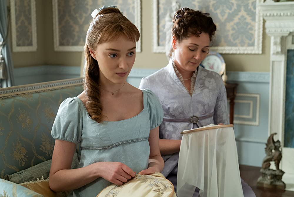 Daphne (Phoebe Dynevor) looking suspicious while she does needlework with her mother, Lady Violet Bridgerton (Ruth Gemmell). (Photo credit: Liam Daniel/Netflix)