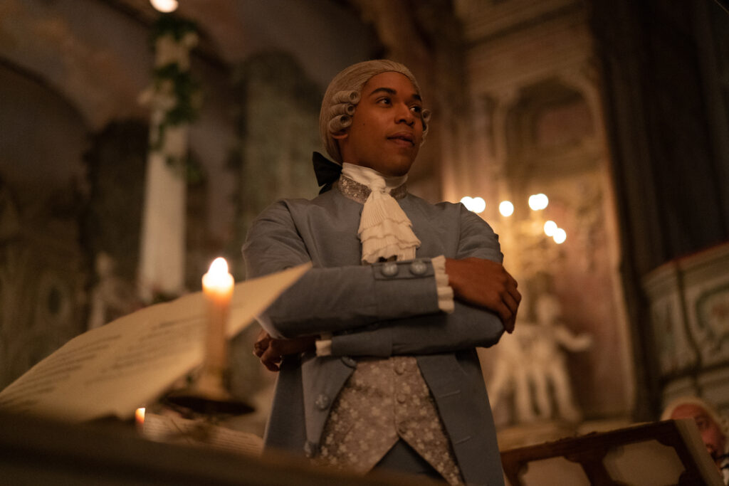 Kelvin Harrison Jr. in the film CHEVALIER. He stands with his arms folded within an orchestra while wearing a blue suit. Photo by Larry Horricks. Courtesy of Searchlight Pictures. © 2023 20th Century Studios All Rights Reserved.