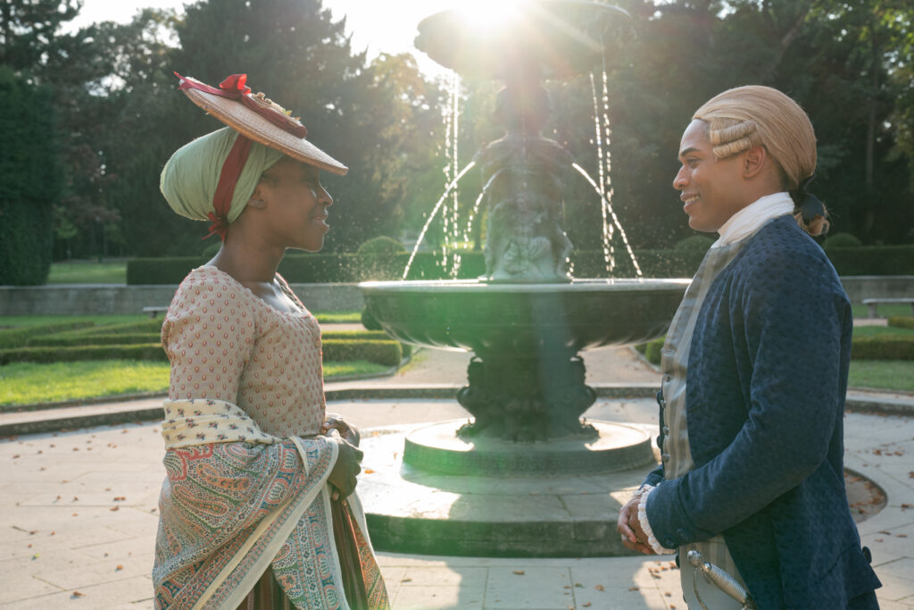 (L-R) Ronke Adekoluejo as Joseph Bologne's mother Nanon and Kelvin Harrison, Jr. as Bologne. They are standing outside near a water fountain. 