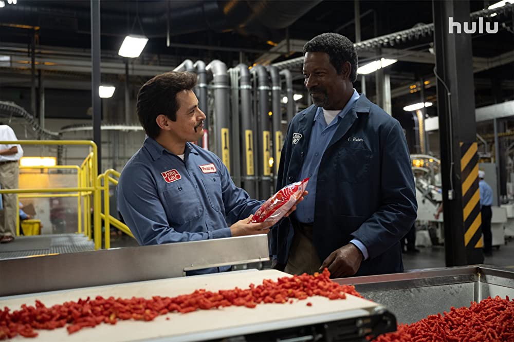 Jesse Garcia and Dennis Haysbert stand next to a line of Flamin' Hot Cheetos